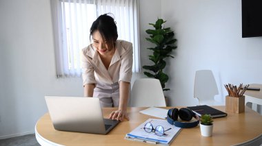 Genç bayan girişimci çalışma alanında duruyor ve dizüstü bilgisayarla çalışıyor..