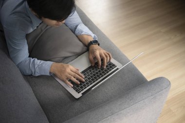 Oturma odasındaki kanepede uzanan ve bilgisayar laptopuyla internette sörf yapan genç bir adamın boy açısı..