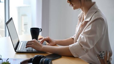 Modern ofiste oturan ve dizüstü bilgisayarla çalışan genç tasarımcının yan görüntüsü.