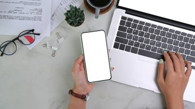 İş kadınının cep telefonu tutarken ve mermer masanın üzerinde dizüstü bilgisayarla çalışırken çekilen bir fotoğrafı..