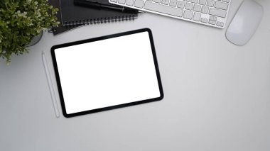 Boş ekran, stilus kalem, klavye ve bitkinin beyaz ofis masasında oluşturduğu dijital öykünün üst görünümü
