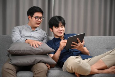 Evdeki kanepede otururken dijital kullanan sıradan homoseksüel çift. Homoseksüel, LGBT kavramı.