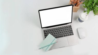 Bilgisayar, dizüstü, defter, kalem tutacağı ve ev bitkisini beyaz ofis masasına yerleştir.
