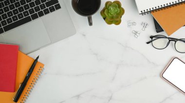 Laptop, kahve fincanı, bardaklar, akıllı telefon ve mermer masadaki not defteri ile rahat çalışma alanı.
