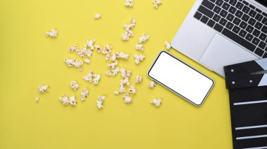 Mock up smart phone, laptop, clapboard and popcorn on yellow background.