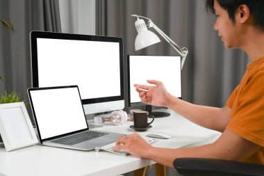 Modern merkez büroda birden fazla cihazla çalışan serbest çalışan genç bir adamın yan görünüşü.