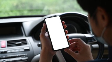 Koruyucu maske takan ve arabasında otururken cep telefonu kullanan Asyalı genç adamın yakın görüntüsü..