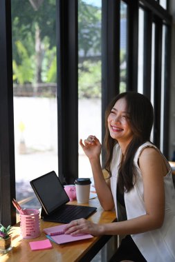 Modern bir iş yerinde oturmuş gülen neşeli genç bir kadının portresi..