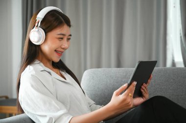 Kulaklık takan ve dijital tabletten bir şeyler izleyen neşeli genç bir kadın..