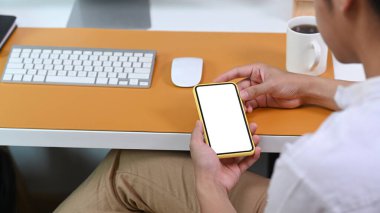 Rear view of casual man sitting at office desk and using smart phone.