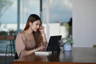 Ofiste otururken bilgisayar tabletleriyle çalışan ciddi bir iş kadını..