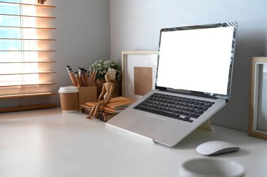 Boş ekranlı bilgisayar bilgisayarı, ev bitkisi, kalem tutacağı ve kahve fincanı ev ofisinin beyaz masasında..