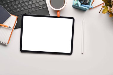 Üst görünüm dijital tablet, kahve fincanı, defter ve kalem tutacağı beyaz ofis masasında..