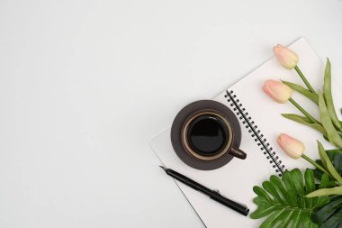 Kahve fincanının, defterin, kalemin, pembe lalenin ve beyaz masadaki fotokopi alanının üstünde..