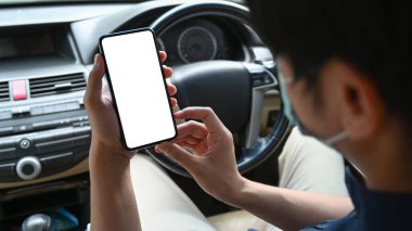 Koruyucu maske takan, arabada oturan ve akıllı telefon kullanan adamın yakın görüntüsü..