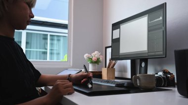 Side view of young female graphic designer working with graphic tablet at modern office.