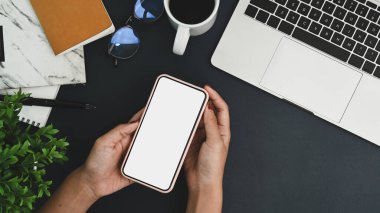 Yukarıda kadın elleri, çalışma alanının üzerinde beyaz ekranlı akıllı telefon taklidi yapıyor..