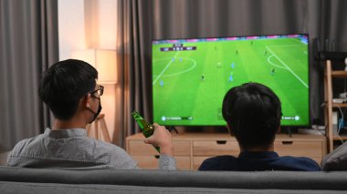 Evde elinde bira bardakları ve tezahürat yapan iki Asyalı genç adam..