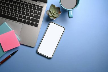 Akıllı telefon, dizüstü bilgisayar, kahve fincanı ve mavi arka planda not defteri..
