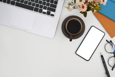 Üst düzey cep telefonu, dizüstü bilgisayar, kahve fincanı, bardaklar ve çiçekler beyaz ofis masasında..