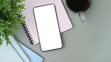 Mock up smart phone with white screen, notebook, coffee cup and house plant o office desk.