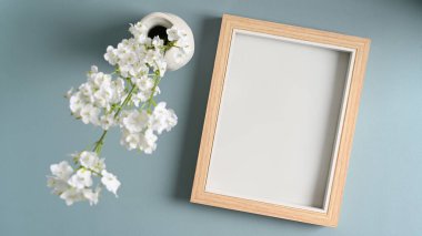 Boş fotoğraf çerçevesi ve mavi çayır arka planındaki vazolarda çiçekler.