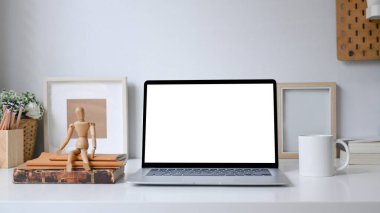 Boş ekranlı ve beyaz masadaki ofis malzemeleriyle öndeki bilgisayar dizüstü bilgisayarı.