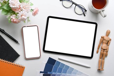Üst görünüm dijital tablet, cep telefonu, gözlük, not defteri ve kahve fincanı beyaz masa üzerinde.