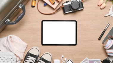 Tahta arka planda dijital tablet ve seyahat aksesuarlarının üst görüntüsü. Tatil kavramı.