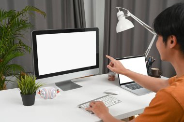 Ofiste otururken bilgisayarın ekranını gösteren genç adamın yan görüntüsü.