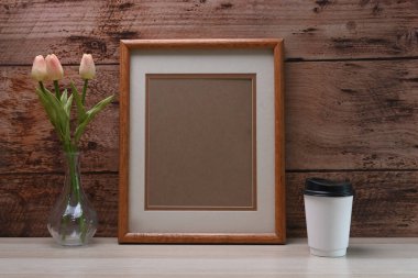 Boş fotoğraf çerçevesi, kahve fincanı ve saksı beyaz masada ve ahşap duvarda..