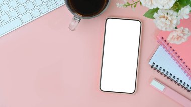 Mock up mobile phone with empty screen, coffee cup, flowers and notebook on pink pastel background.