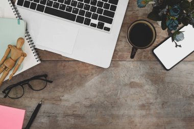 Dizüstü bilgisayarlı, cep telefonlu, ahşap masadaki defter reklamlı çalışma alanı..