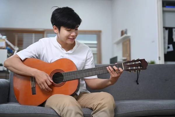 Happy Young Man Playing Guitar While Siting Comfortable Sofa Home — Stock fotografie