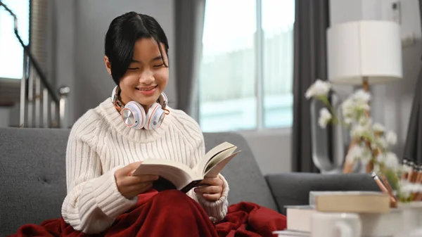 快乐的女孩 带着耳机在沙发上看书 — 图库照片