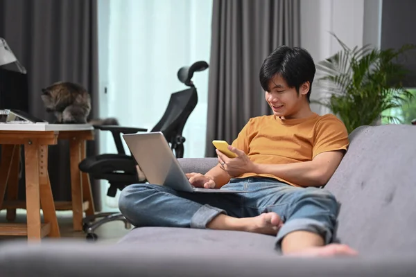 Casual Man Sitting Sofa Using Laptop Computer Mobile Phone — Φωτογραφία Αρχείου