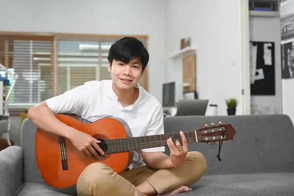 Feliz Jovem Asiático Homem Sorrindo Sentado Com Sua Guitarra Sofá — Fotografia de Stock