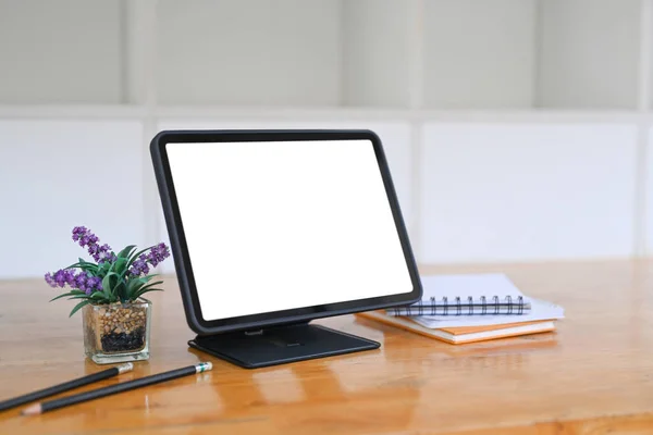 Digital tablet with blank screen, notebook and house plant on wooden desk.