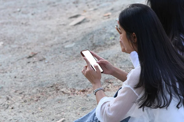 Two Young Asian Woman Sitting Outdoor Using Mobile Phone — Stok fotoğraf