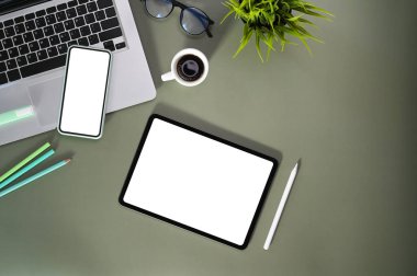 Boş ekranlı akıllı telefon, tablet, gözlük, dizüstü bilgisayar ve kırtasiye malzemeleriyle çağdaş çalışma alanının üst görünümü.