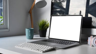 Boş ekran, klavye, bitki ve kahve fincanı beyaz masada olan bilgisayar ile modern çalışma alanı.