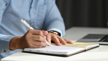 Not defterine yazarken ve işyerinde otururken elinde kalem tutan işadamının yakın görüntüsü.