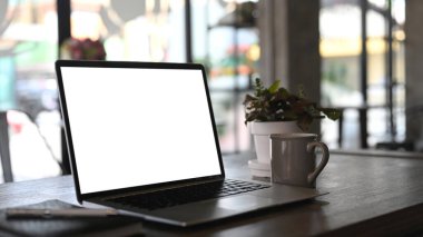 Bulanık ofis odası arka planına sahip ahşap masanın üzerinde boş ekran laptopuyla basit çalışma alanı.