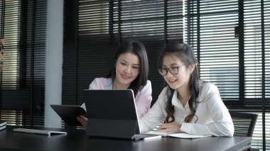 İş kadını, genç bir meslektaşıyla modern bir iş salonunda bilgi tartışmak için dijital tablet kullanıyor..