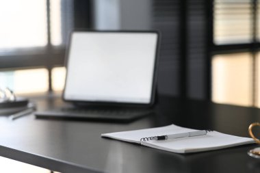Bir defter ve kalem, siyah tahta masa üzerinde boş ekran bilgisayar dizüstü bilgisayarıyla çağdaş çalışma alanına yerleştiriliyor..