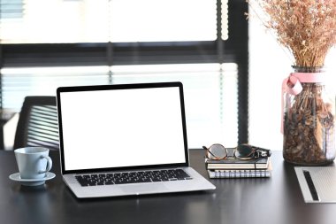 Boş bir dizüstü bilgisayar, kahve fincanı, ev bitkisi, defter ve gözlükler siyah ahşap masa üzerinde. Ürün montajı için boş ekran..