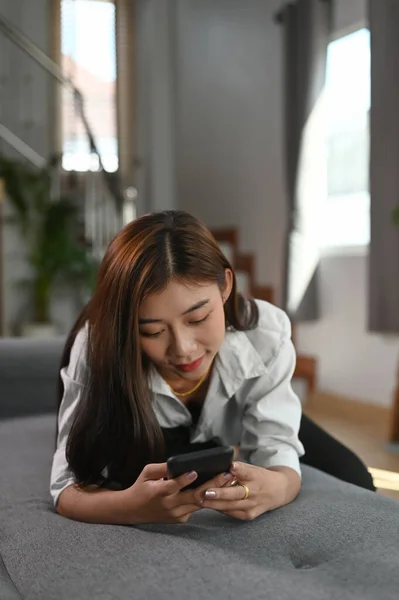 Młoda Kobieta Leży Kanapie Korzysta Smartfona Przeglądającego Internet Domu — Zdjęcie stockowe
