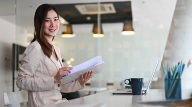 Çekici bir iş kadını kameraya gülümsüyor ve çalışma alanında çalışıyor..