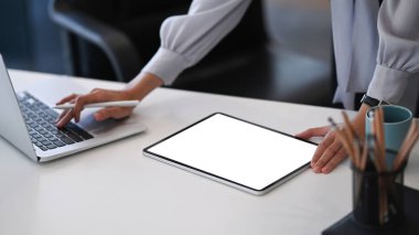 Dijital tablet kullanan ve ofisteki dizüstü bilgisayarda arama yapan genç bayan tasarımcı.