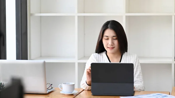 若い女性のフロントビューは 現代のオフィスに座っている間タブレットコンピュータ上で作業に集中 — ストック写真